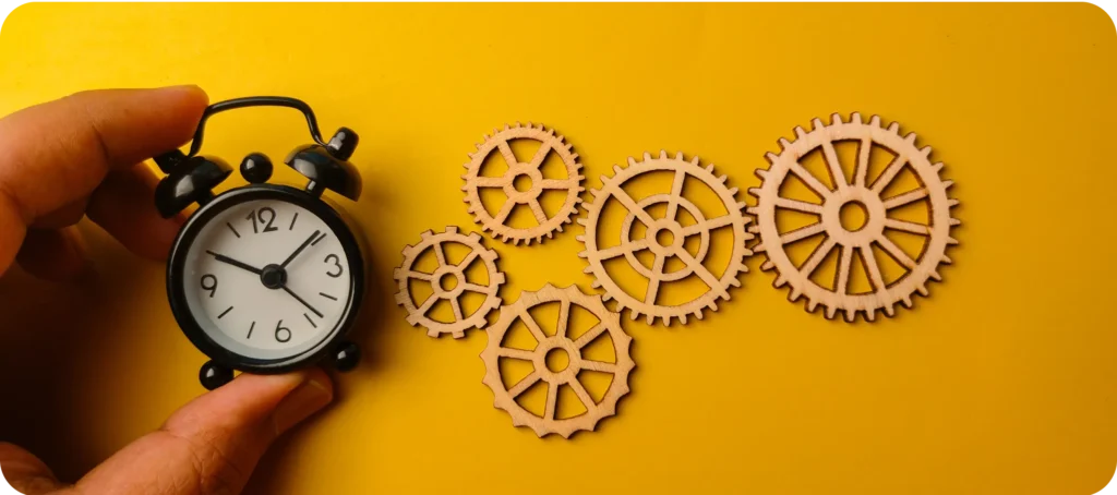 Hand holding alarm clock with wooden gear on a yellow background