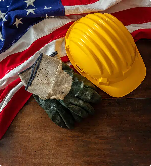 Construction safety gear, including a yellow hard hat and work gloves, displayed on an American flag